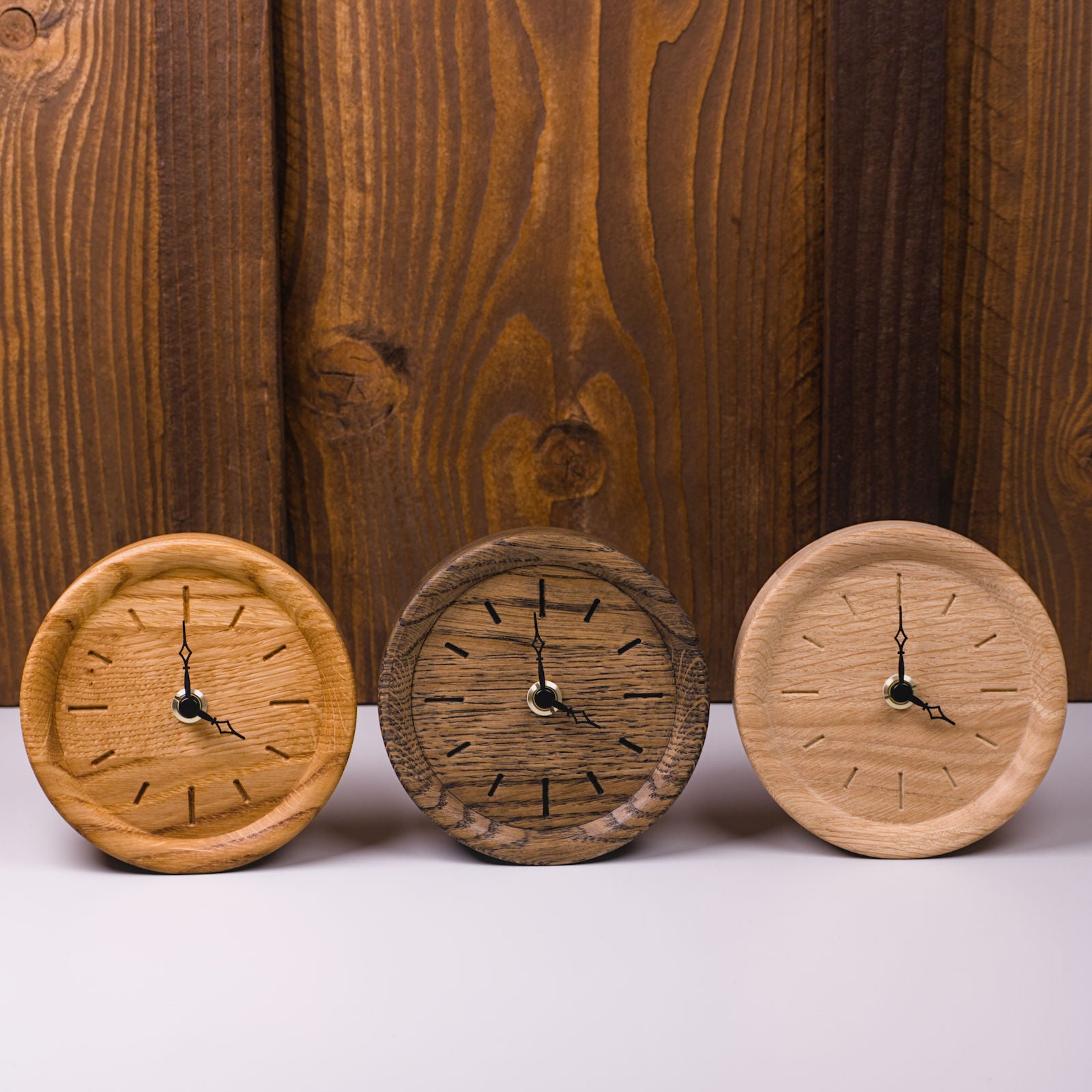 Drei runde Standuhren in den Varianten Rohholzeffekt, klassisch geölt und colour geölt – nebeneinander aufgestellt, handgefertigt im Solothurner Unterleberberg von HolzPart.